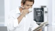 Un homme buvant un expresso pendant qu'il lit le journal